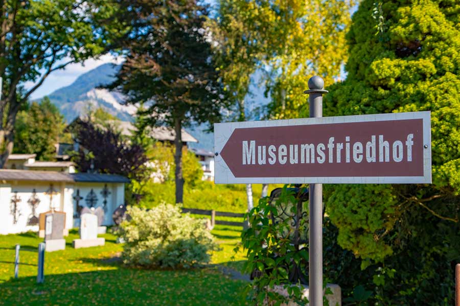 Straßenschild auf dem "Museumsfriedhof" steht, Natur und ein weißes Haus im Hintergrund