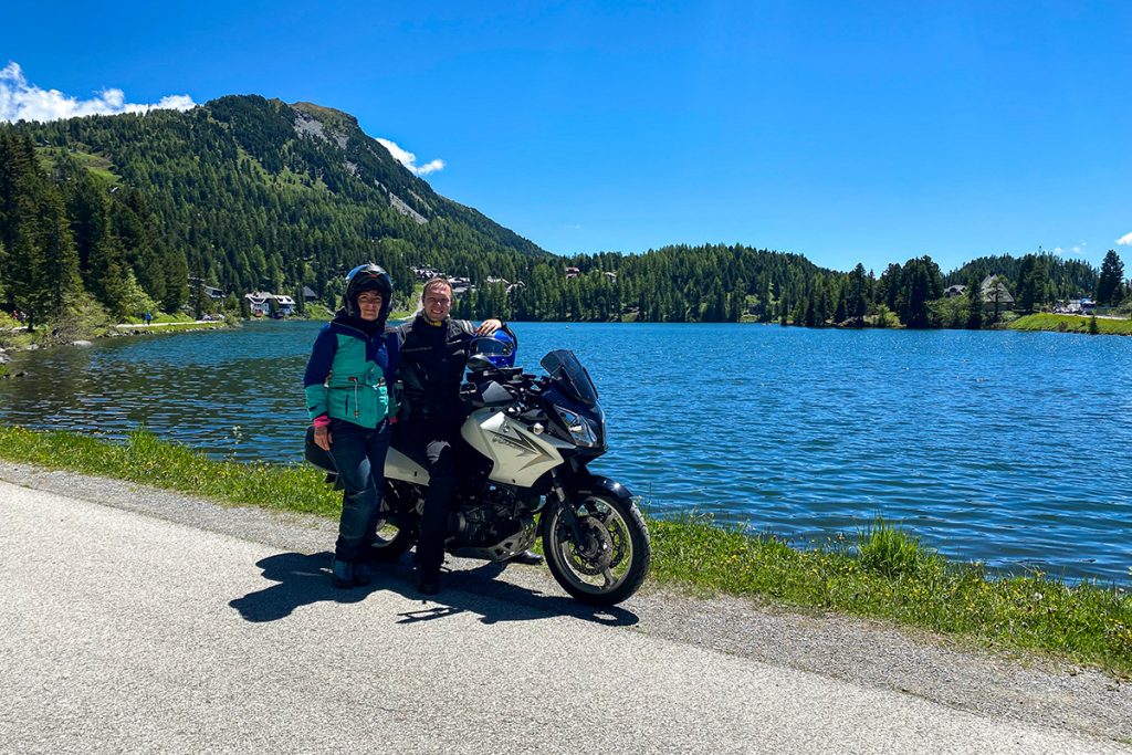 Pärchen auf Motorrad vor See und Berg im Hintergrund