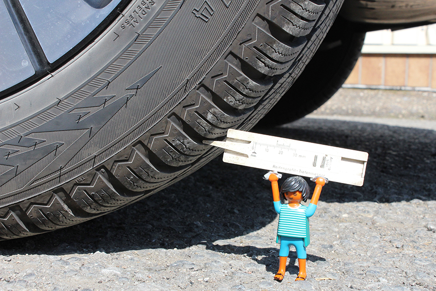 Playmobilemännchen das mit einem Messgerät die Profiltiefe eines Reifen misst