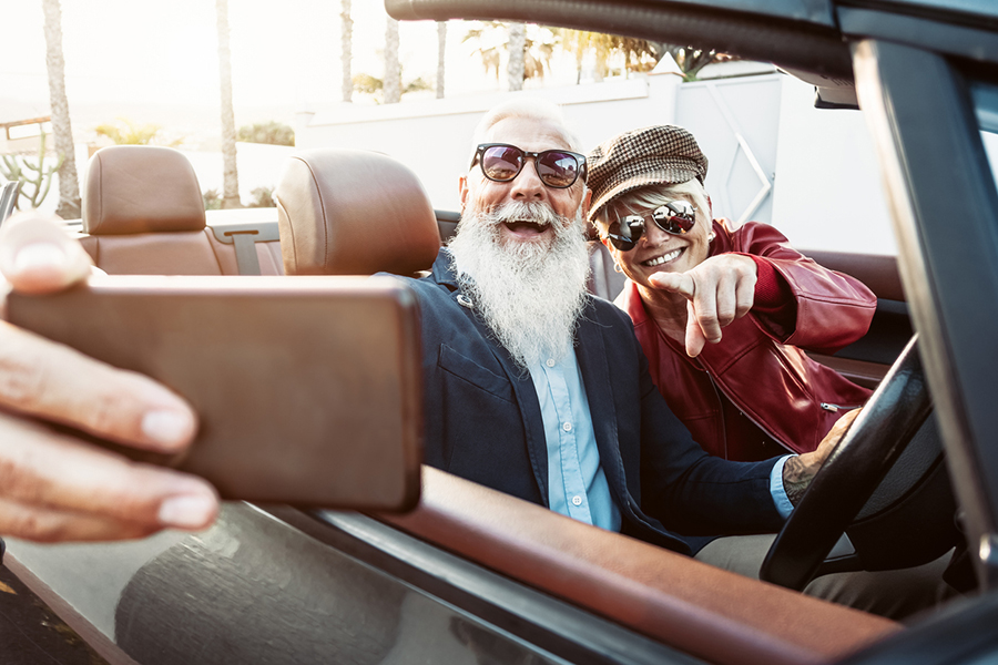 Mann mit weißem Bart und Frau mit roter Lederjacke machen ein Selfie im Auto