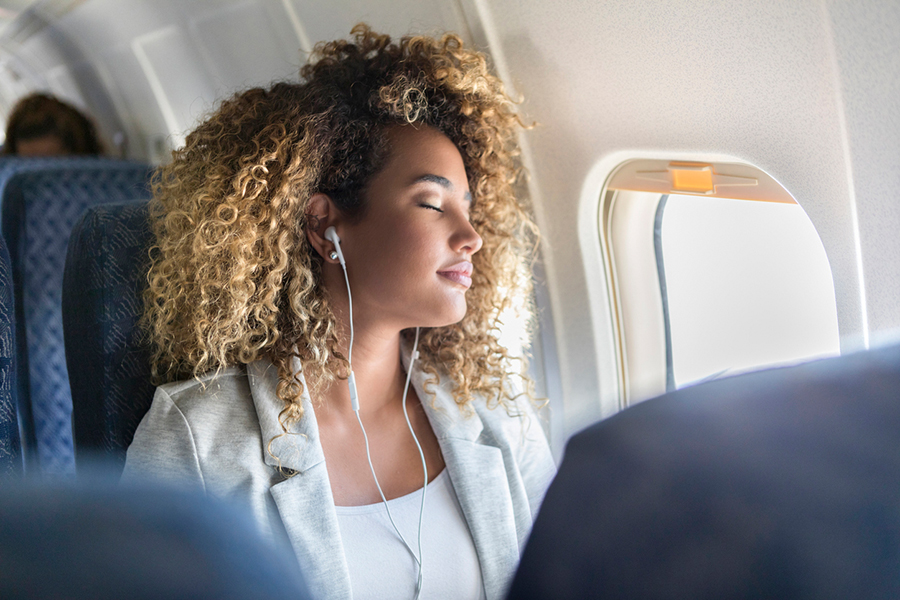 Frau sitzt mit Kopfhörern im Flugzeug und hat Kopfhörer in den Ohren
